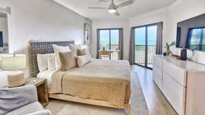 A modern hotel room with a bed, bedside table, lamp, and a view of the sea through large windows.