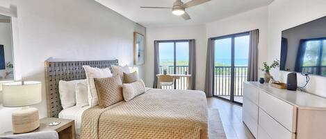 A modern hotel room with a bed, bedside table, lamp, and a view of the sea through large windows.