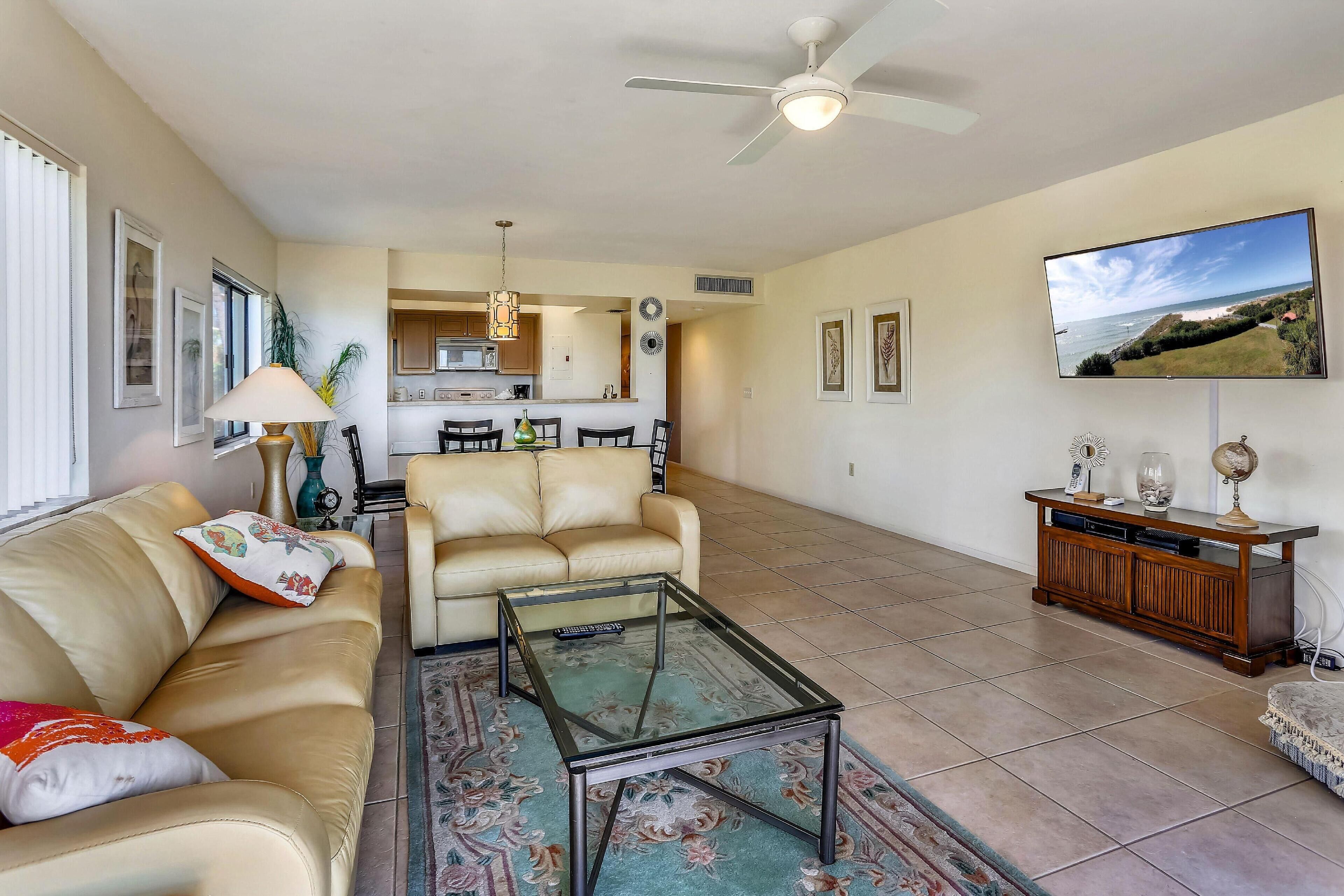A living room with a sofa, coffee table, and TV. There is a kitchen in the background.