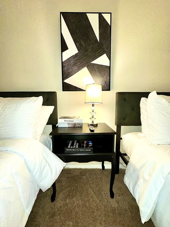 A hotel room with two beds, a nightstand with a lamp, a book titled "Persiana," and a framed picture on the wall. - Steps from Fondren’s Favorite Spots: 5 minutes from Hospital’s (Jackson)