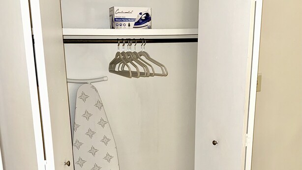 A bedroom with a bed, a closet with hanging clothes, and a shelf with a box.