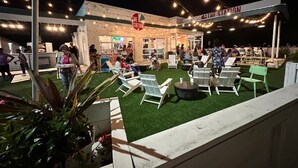An outdoor seating area with white chairs and tables, a gas station sign, and string lights.
