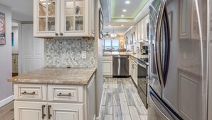 A kitchen with white cabinetry, a tiled backsplash, and stainless steel appliances. - Land's End 11-405 Beach Front - Premier (Treasure Island)