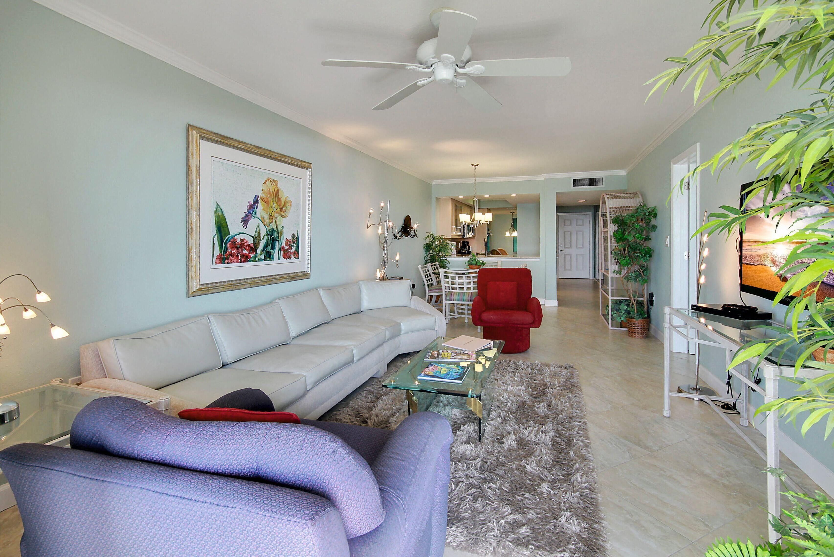 A living room with a sofa, a red chair, a glass coffee table, and a ceiling fan.