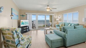 A living room with a sofa, armchair, and a coffee table. There is a TV and a sign for Resort Rentals.