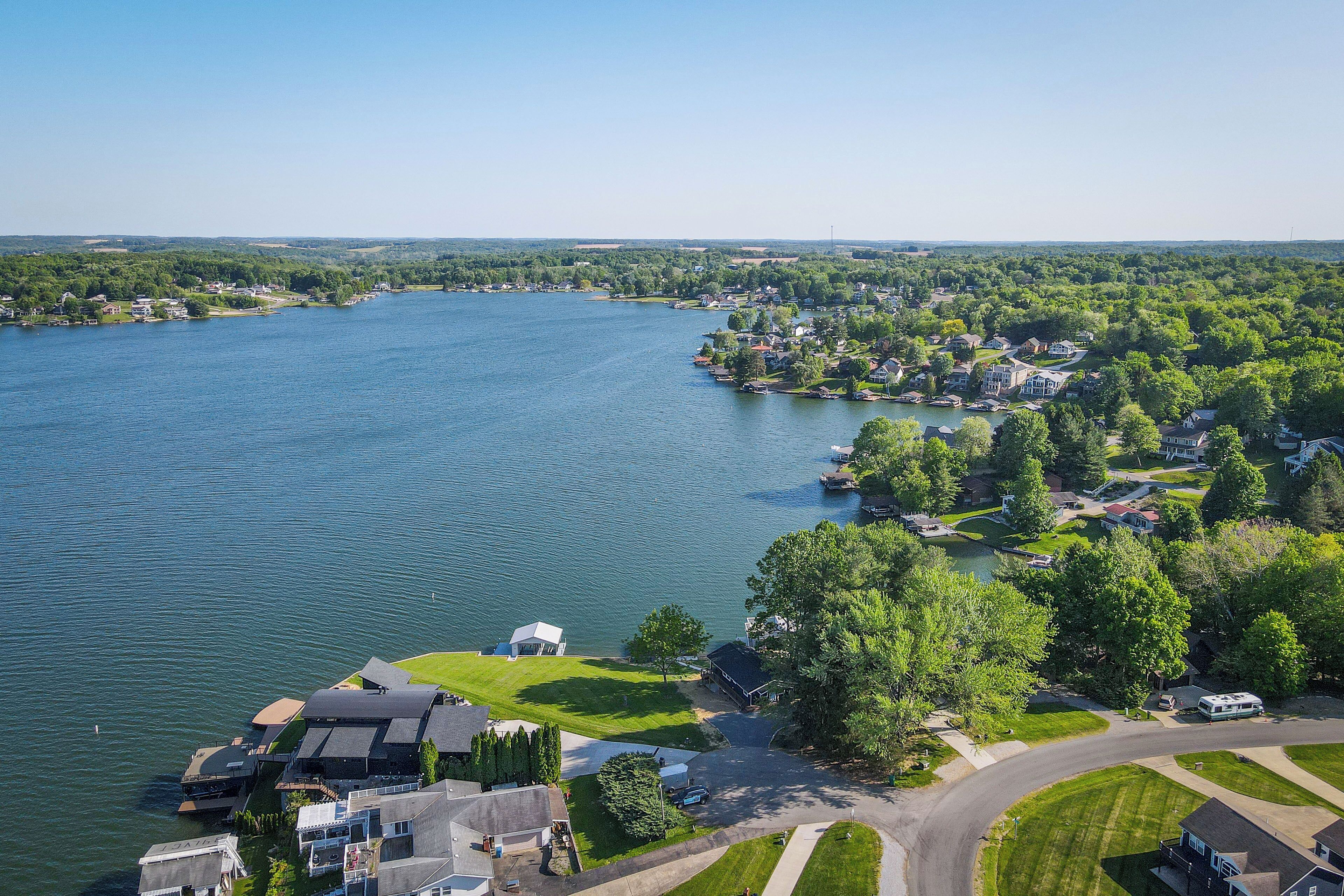 An aerial view of a lakeside residential area with houses, a marina, and a large white building with a green lawn.