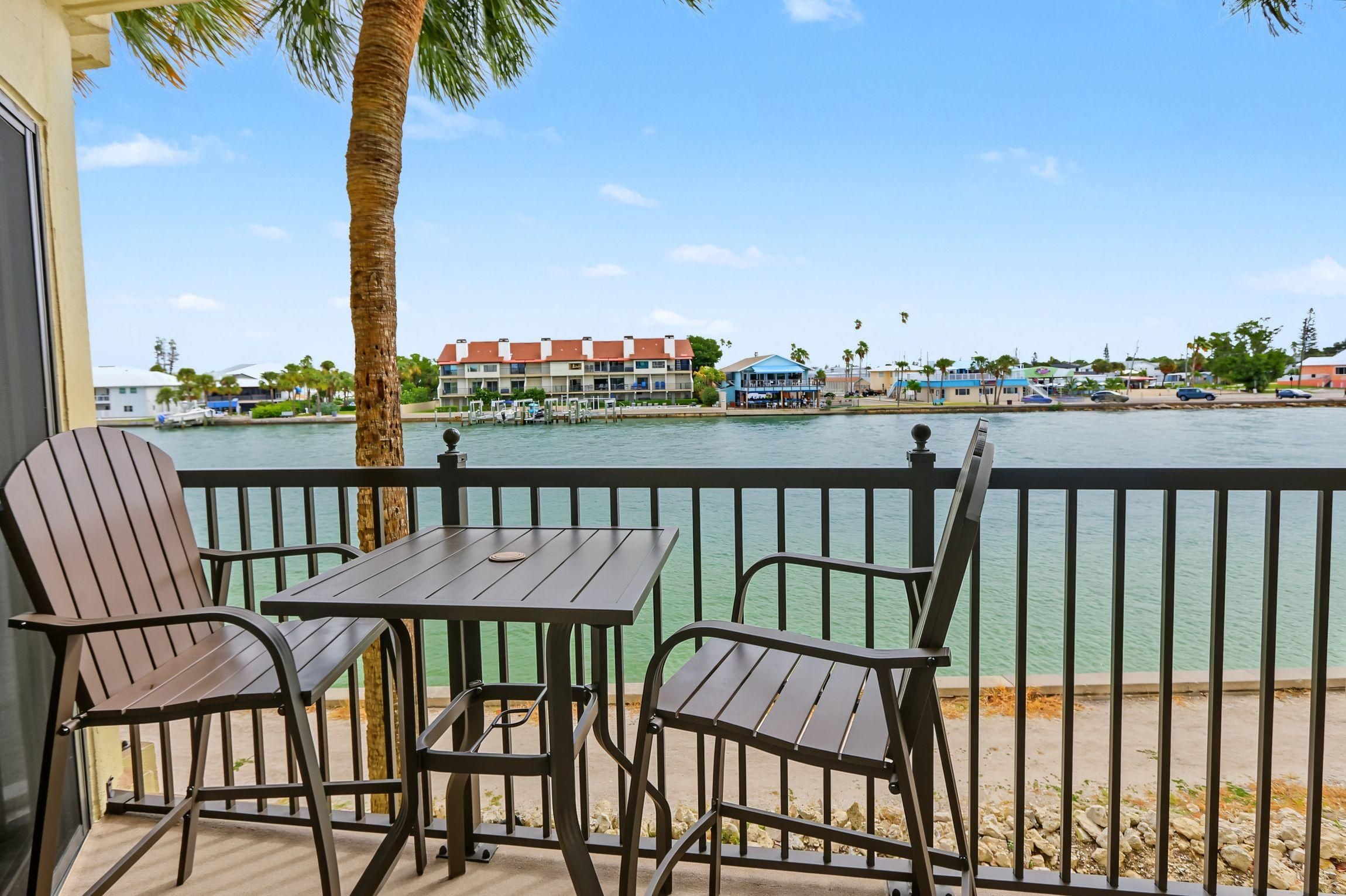 Een balkon met een tafel en stoelen, met uitzicht op een waterkant met gebouwen op de achtergrond.