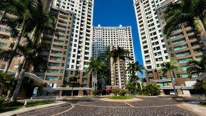 A modern high-rise hotel with a central courtyard, palm trees, and a clear blue sky.