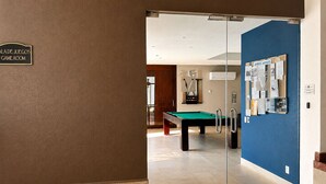 A game room with a pool table, a billiards rack, and a glass door leading to a hallway.
