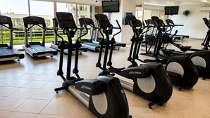 A gym with multiple cardio machines, a TV, and a large window with a view of greenery.