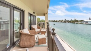 A balcony with wicker furniture, a view of a calm body of water, and a distant shoreline with buildings. - Land's End 3-301 Bay Front - Premier (Treasure Island)