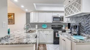 A modern kitchen with white cabinets, a black microwave, and a teal backsplash.