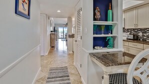 A hallway with a kitchen area featuring white cabinets, a granite countertop, and a decorative shelf with vases. - Land's End 4-303 Bay Front - Premier (Treasure Island)