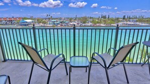 A balcony with three chairs and a table, overlooking turquoise waters and a marina with boats and buildings. - Land's End 4-406 Bay Front (Treasure Island)