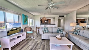A living room with a sofa, a coffee table, a TV on a white stand, and a ceiling fan. - Land's End 4-406 Bay Front (Treasure Island)