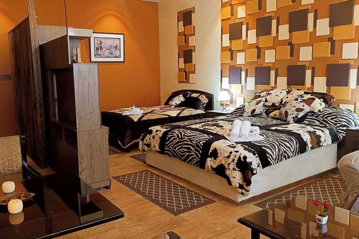 Une chambre d’hôtel avec deux lits, une armoire en bois, une petite table avec des bougies et un panneau décoratif au mur.