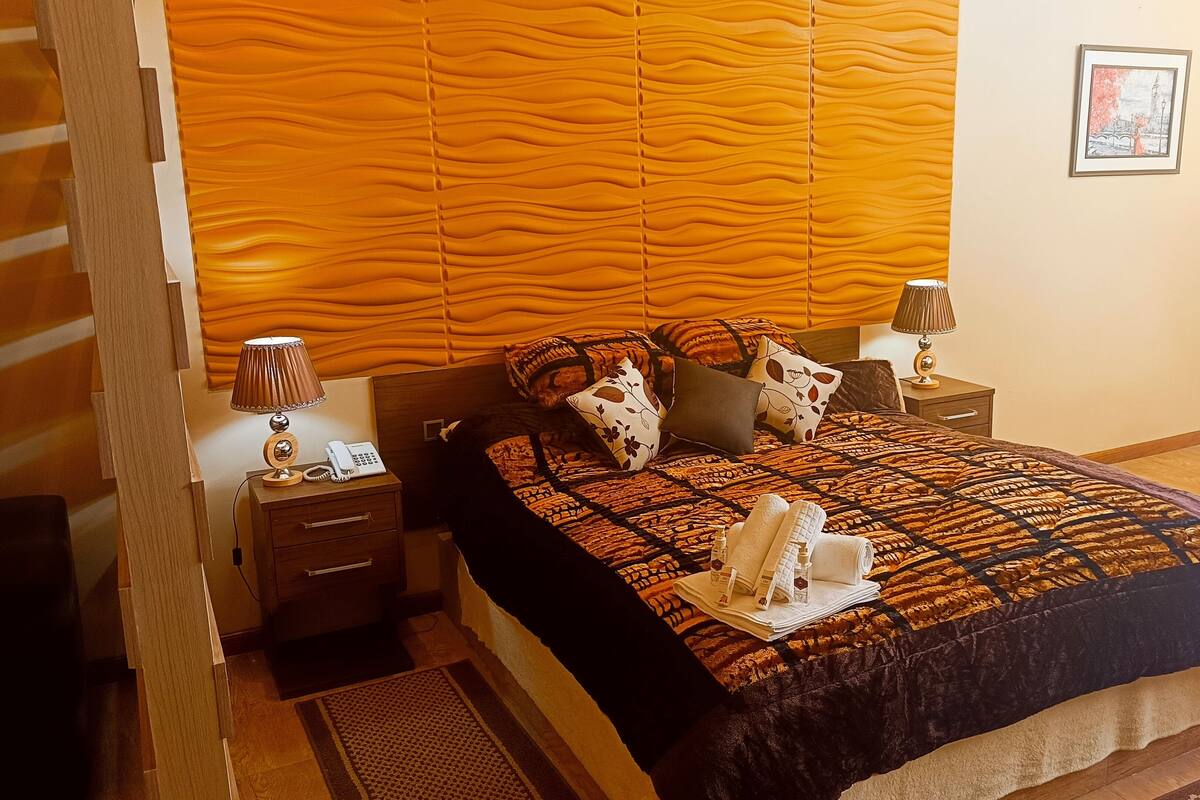 Une chambre d’hôtel avec un lit, deux tables de chevet, une commode, une lampe, un téléphone et un tableau encadré au mur.