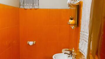 Ein kleines Badezimmer mit orangefarbenen Fliesen, einer weißen Toilette, einem Standwaschbecken und einem Spiegel mit einem darüberhängenden Handtuch.