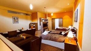 Habitación de hotel compacta con comedor, una cama con colcha estampada, televisión y una pequeña kitchenette.