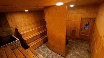 A wooden sauna room with benches and a door leading to a smaller area with a window and red buckets.