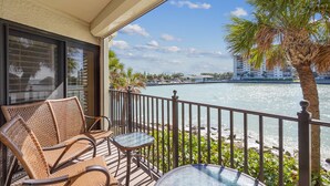 A balcony with wicker furniture, a glass table, and a view of a river and buildings. - Land's End 5-202 Gulf-bay Front - Premier (Treasure Island)
