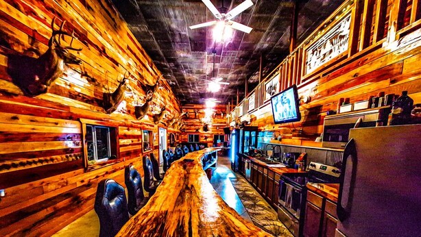 Eine Bar mit Holzwänden, einer langen Theke und Barhocker.