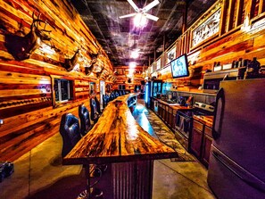Een bar met houten wanden, een lange toonbank en barstoelen.