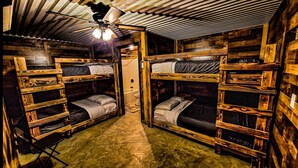 Ein kompakter, rustikaler Raum mit Etagenbetten, einem Deckenventilator und einem kleinen Badezimmer.