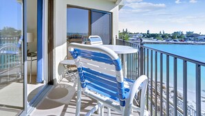 Ein Balkon mit Tisch und einem blauen und weißen Stuhl, mit Blick auf Strand und Stadtlandschaft.