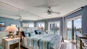 Ein Schlafzimmer mit Bett, Nachttischen, Deckenventilator und Blick ins Freie.