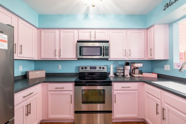Una cocina con gabinetes rosados, un refrigerador de acero inoxidable, un microondas, una estufa y una cafetera.