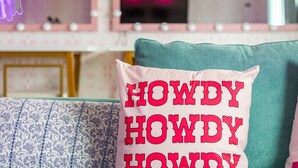 En tealgrøn sofa med dekorative puder, et neonskilt med teksten "Long Live Cousins" og et spejl med lys.