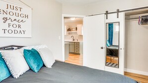 Een slaapkamer met een bed, een schuifdeur naar een badkamer en een keuken die door een open deur zichtbaar is.