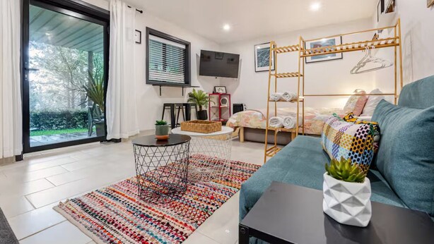 A modern living room with a sofa, a coffee table, a TV, and a balcony with a view of greenery.