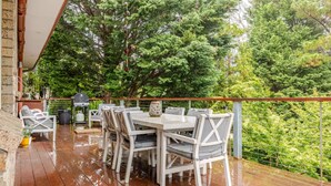 An outdoor patio with a wooden deck, white furniture, and a view of dense greenery.