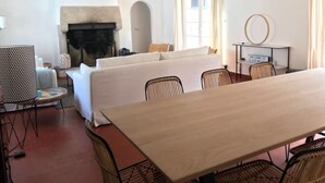 Ein Zimmer mit Kamin, einer Sofagarnitur, einem Esstisch und Korbstühlen.
