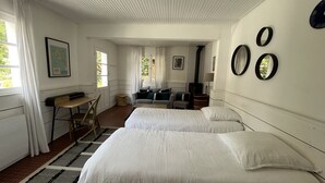 Ein Hotelzimmer mit zwei Betten, einem Schreibtisch, einem Stuhl, einem kleinen Tisch, einer Lampe und einem Fenster mit Vorhängen.