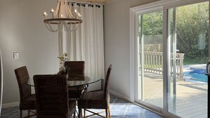 A dining area with a round glass table, wicker chairs, a chandelier, and a view of a backyard with a pool. - Cozy cottage located in the heart of the Mayport fishing village. Pool & Patio! (Jacksonville)