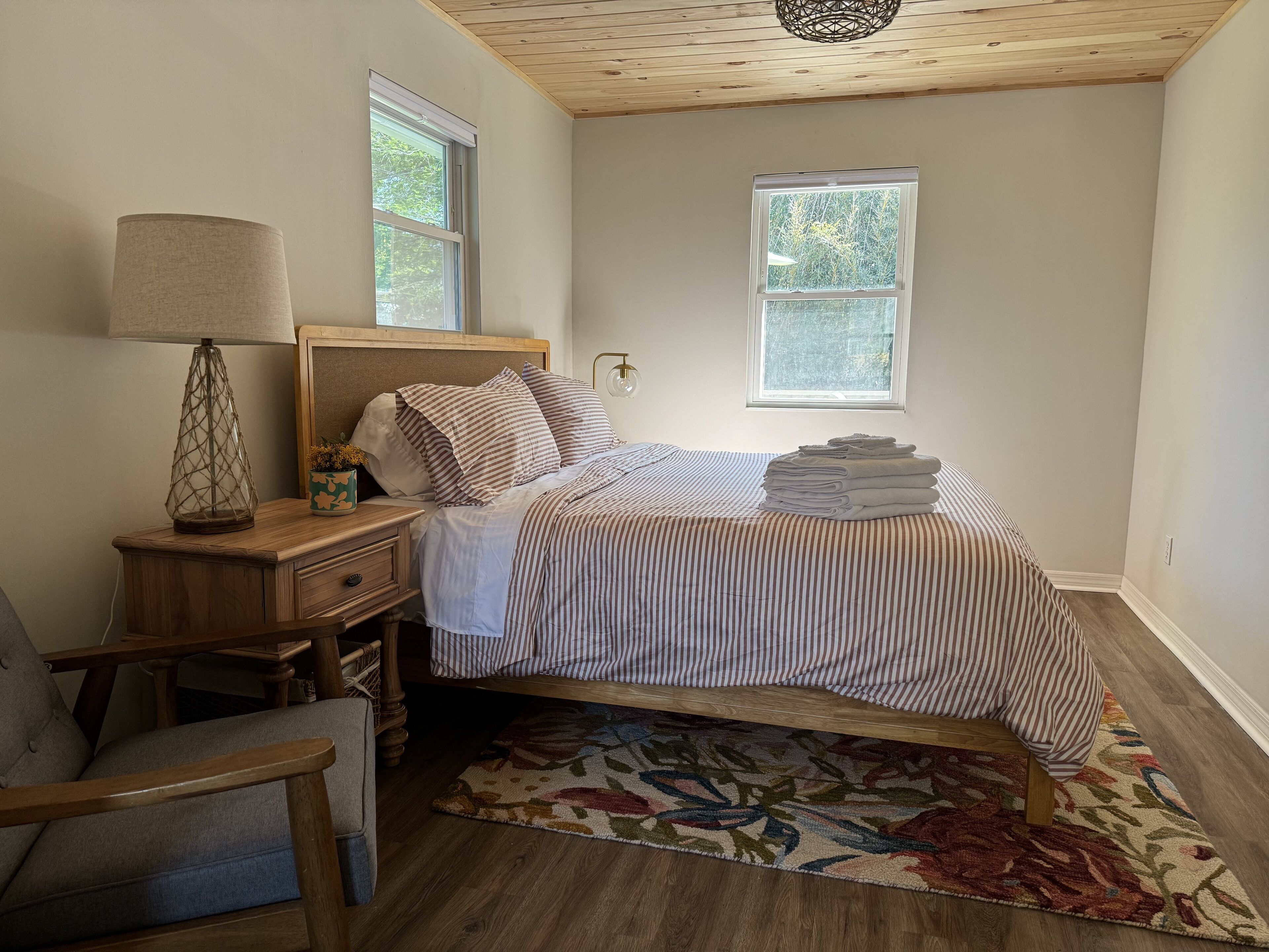 Une chambre à coucher avec un lit, une table de chevet, une lampe, une chaise et une fenêtre.
