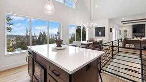 A modern kitchen with large windows, a central island, and a dining area with a fireplace. - Lake Views | Modern & Luxurious | Walk to Town (Lakeside)