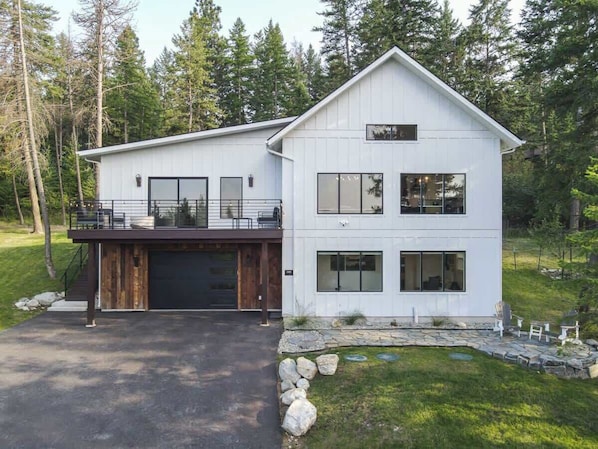 A modern two-story house with a garage, large windows, and a stone pathway leading to the entrance. - Lake Views | Modern & Luxurious | Walk to Town (Lakeside)