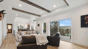 A spacious living area with a modern design, featuring a large sofa, a coffee table, and a view of the outdoors through large sliding glass doors. - Lake Views | Modern & Luxurious | Walk to Town (Lakeside)