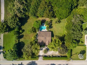 Vista aérea de una propiedad con piscina, rodeada de exuberante vegetación y un camino de entrada pavimentado.