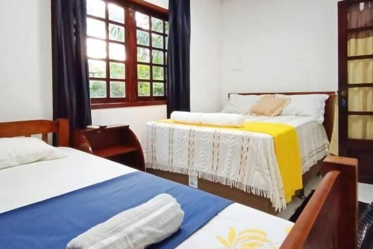 A hotel room with two beds, a wooden headboard, a window with curtains, and a door with a glass panel.