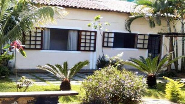 Ein Haus mit einem Ziegeldach, zwei Fenster mit Rollläden und ein Garten mit verschiedenen Pflanzen und einer Bank.
