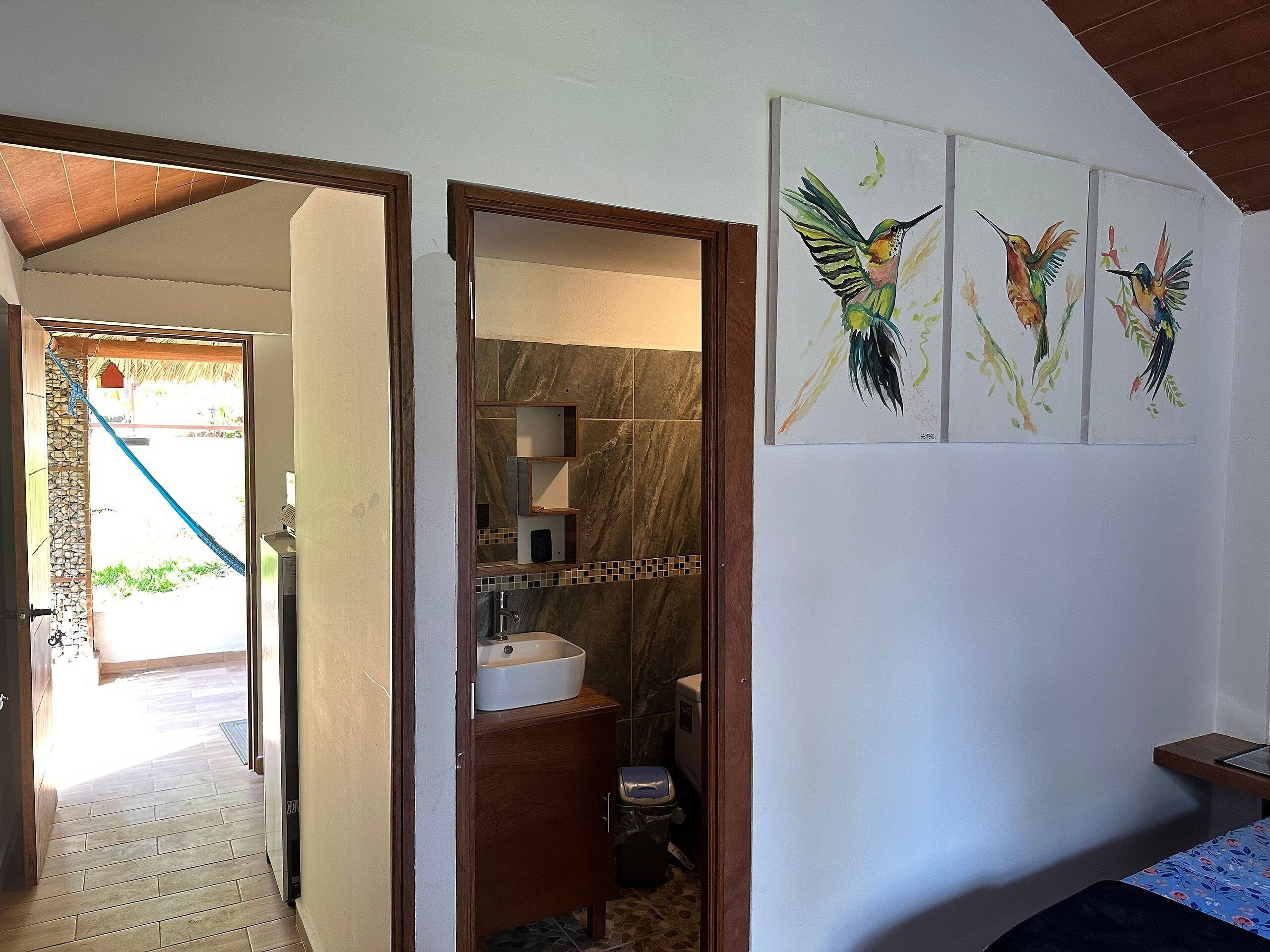 Een badkamer met een marmeren muur, een wastafel en een toilet. Drie ingelijste afbeeldingen van kolibries hangen aan de muur.