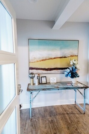 A reception desk with a painting above it, a vase with flowers, and a door to the left.