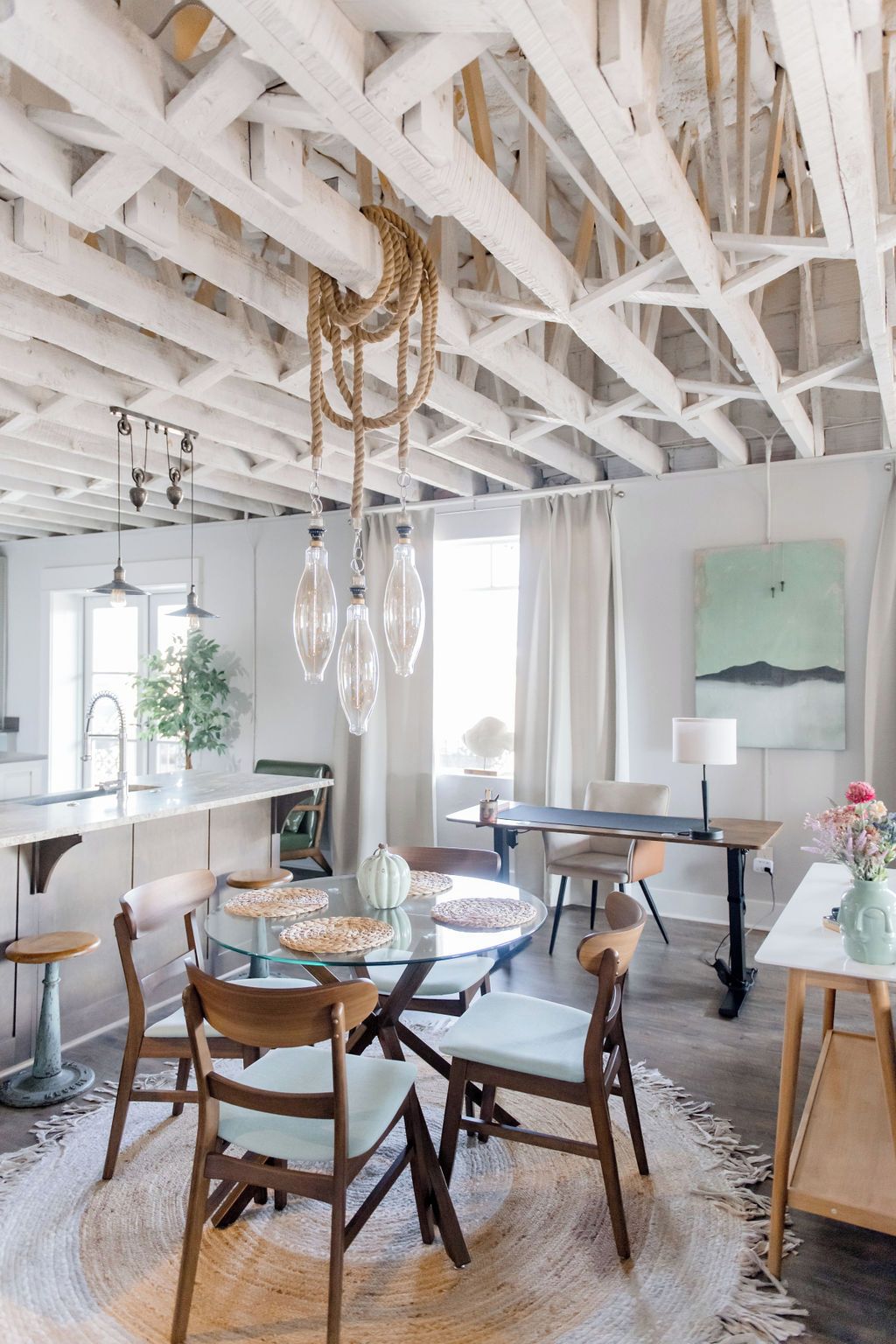 Un espace repas avec une table en verre, des chaises en bois et un plafond avec des poutres apparentes.