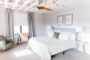 Ein Hotelzimmer mit Bett, Stuhl, Nachttisch und Deckenventilator.