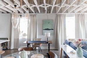 Ein modernes Wohnzimmer mit Essbereich, ausgestattet mit Holzboden, einem Gemälde an der Wand und einem Sofa mit Blumen.'